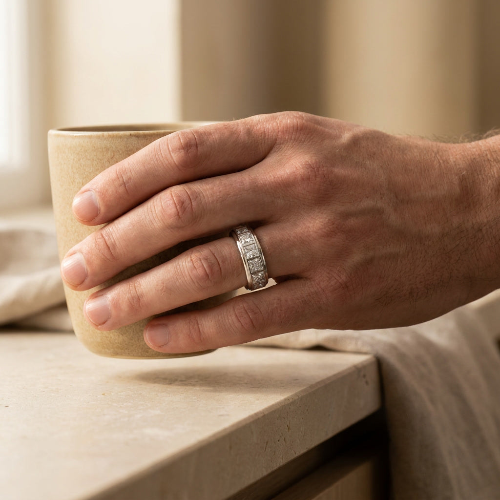 Man's hand wearing the BASTION 10mm princess cut diamond band while lifting a ceramic cup